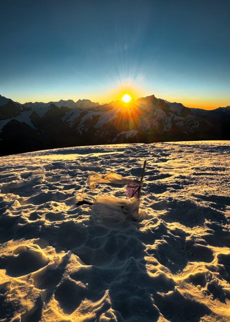 Sonnenaufgang über verschneiten Bergen mit schimmerndem Schnee im Vordergrund.