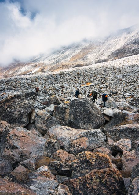 Wanderer über felsigen Boden, umgeben von Bergen und Wolken.