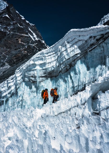 Zwei Bergsteiger mit orangefarbenen Rucksäcken auf einem Gletscher in den Bergen.