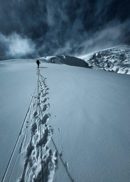 Eine Person erklimmt einen schneebedeckten Hang mit Fußspuren im Schnee.