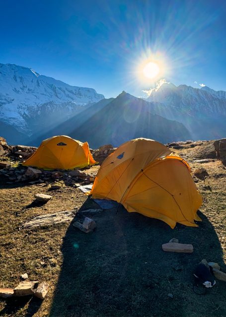 Zwei gelbe Zelte vor einer beeindruckenden Berglandschaft im Sonnenschein.