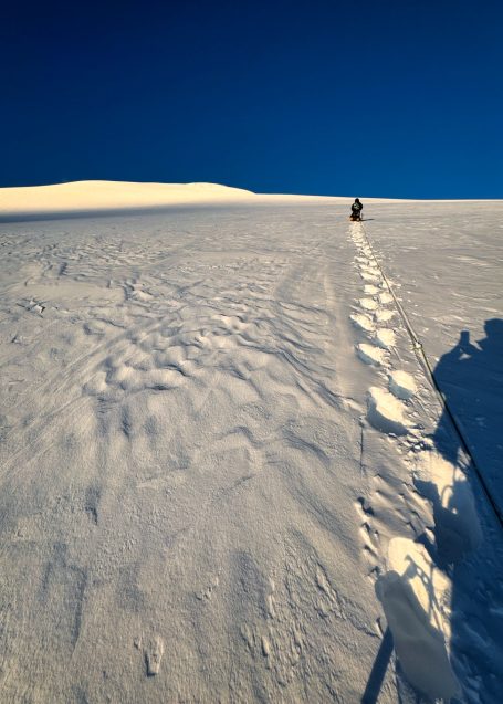 Die Szene zeigt eine Person, die durch eine verschneite Landschaft wandert.