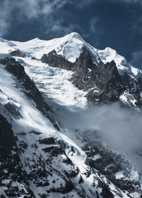 Schneebedeckter Berggipfel mit dramatischem Himmel und Nebel.