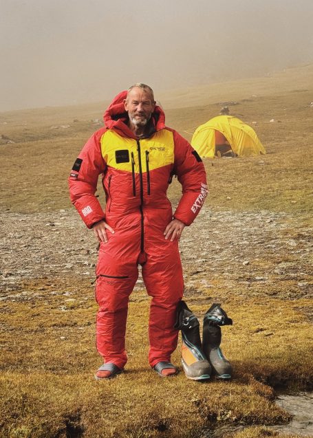 Person in rotem, gefüttertem Anzug steht auf einer Wiese mit Zelt im Hintergrund.