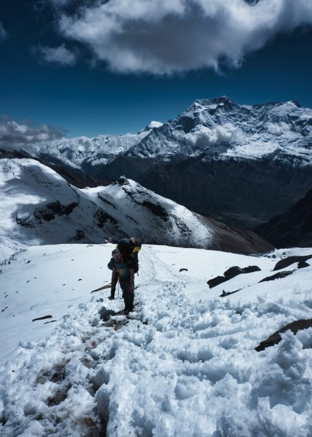 Person wandert durch verschneite Berge unter einem klaren, blauen Himmel.