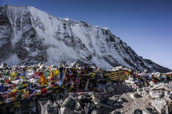 Bunte Gebetsfahnen vor schneebedeckten Gipfeln in einer Berglandschaft.