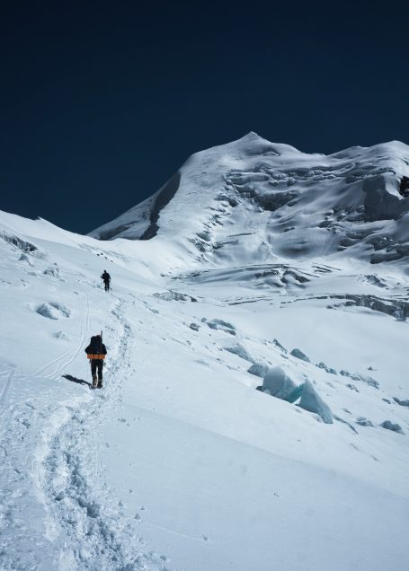 Zwei Personen wandern auf schneebedecktem Gelände mit Berg im Hintergrund.