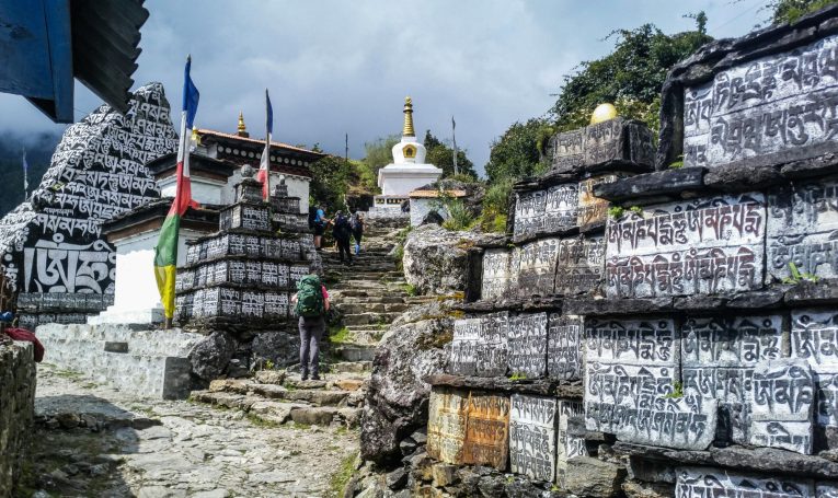Buddhistische Stupa umgeben von gestapelten Steinen mit Inschriften und Gebetsfahnen.