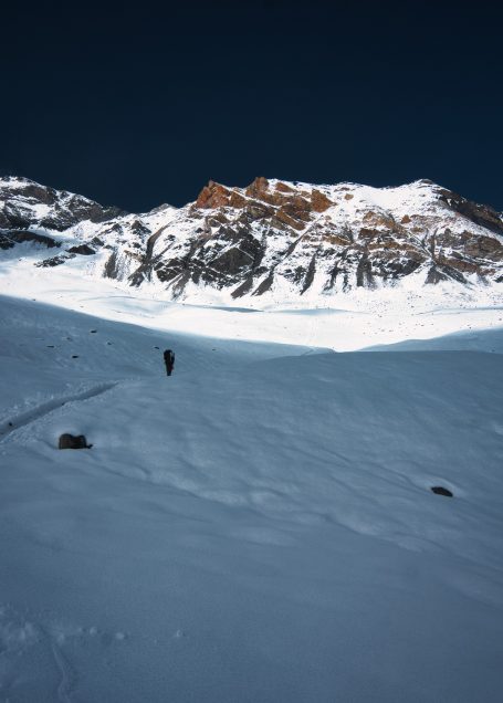 Schneebedeckte Landschaft mit einem Berg im Hintergrund und einer einzelnen Person im Vordergrund.