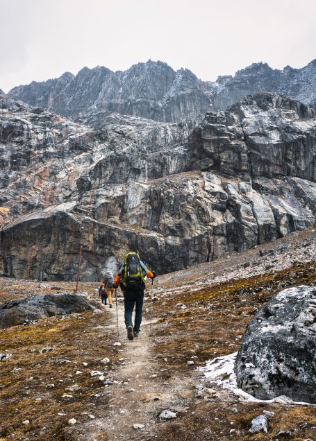 Wanderer auf einem schmalen Pfad in felsiger, gebirgiger Landschaft.