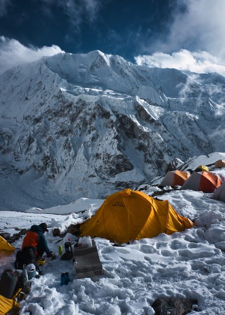 Bunte Zelte auf schneebedecktem Gelände mit beeindruckenden Berggipfeln im Hintergrund.