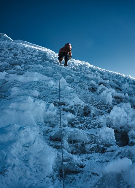 Ein Bergsteiger klettert eine eisige Steilhose unter klarem, blauem Himmel.