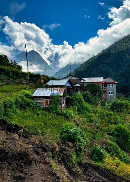 Berglandschaft mit einem Wohnhaus umgeben von üppigem Grün und dramatischem Himmel.