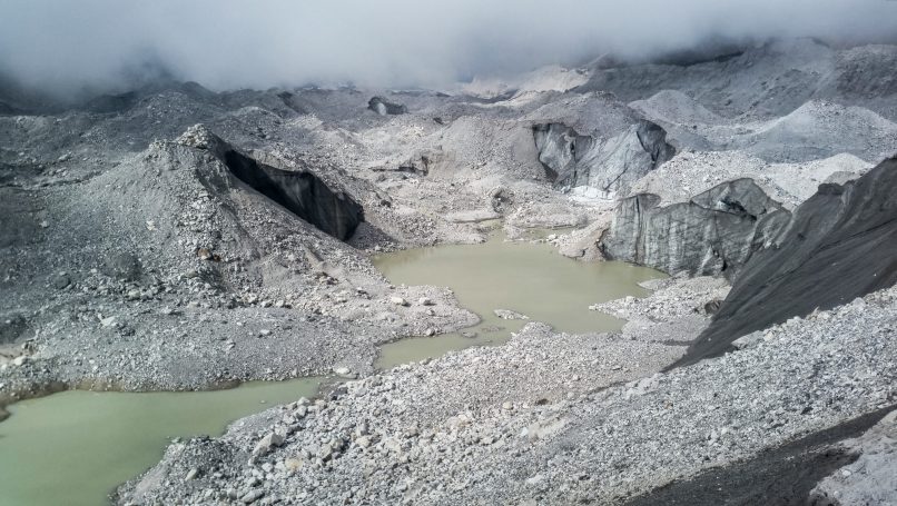 Graue, felsige Landschaft mit einem grünlichen See in einem Vulkanbereich.