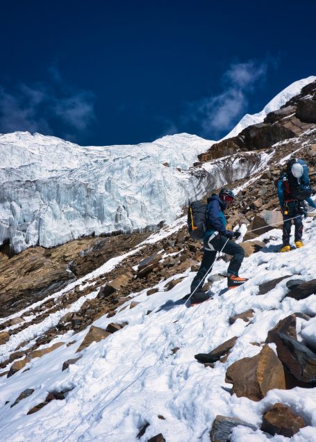 Zwei Bergsteiger im Schnee, umgeben von eisigen Felsen und blauen Himmel.