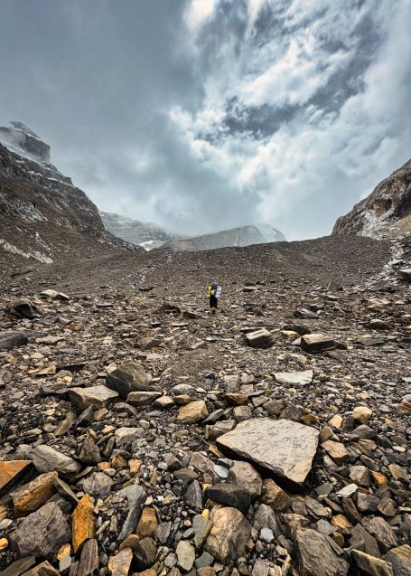 Ein Mensch steht auf einer steinigen Hochebene mit bewölktem Himmel im Hintergrund.