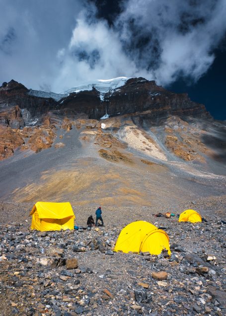 Gelbe Zelte auf felsigem Gelände mit schneebedecktem Berg im Hintergrund.