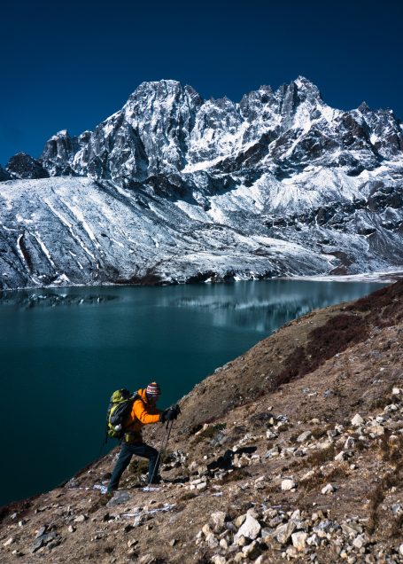 Bergsteiger mit Rucksack wandert in gebirgiger Landschaft mit schneebedeckten Gipfeln.