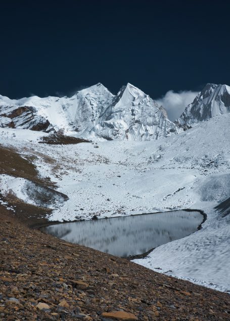 Schneebedeckte Berge mit einem stillen See im Vordergrund, klarer blauer Himmel.