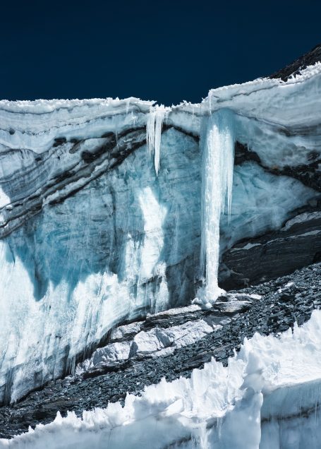 Eisige Felswand mit hängenden Eiszapfen und glitzerndem Gletscher.