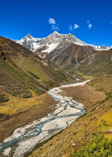 Berglandschaft mit schneebedeckten Gipfeln und einem glitzernden Fluss im Tal.