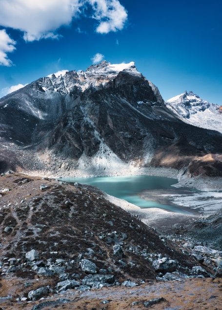 Berglandschaft mit einem glitzernden See im Tal und schneebedeckten Gipfeln.