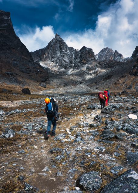 Bergsteiger wandern durch eine felsige Landschaft mit dramatischem Himmel.