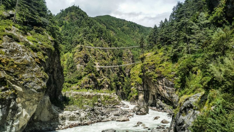 Grüne Berglandschaft mit einem Fluss und einer hohen Hängebrücke.