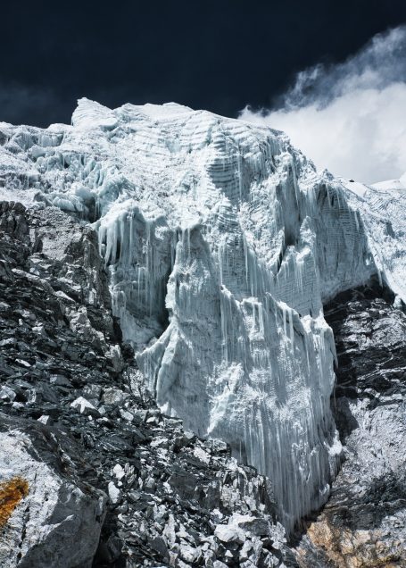 Eisgletscher mit steilen Felsen und dunklem Himmel im Hintergrund.