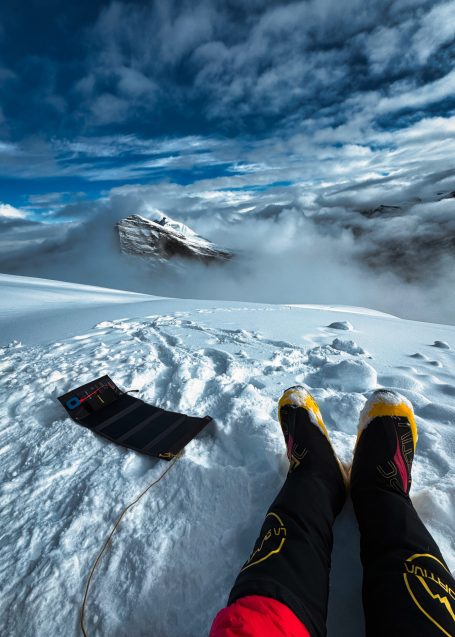 Füße in Schneelandschaft mit Bergen und bewölktem Himmel im Hintergrund.