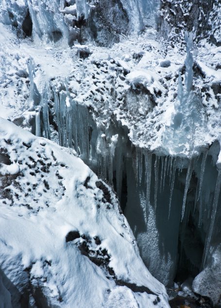 Eiszapfen hängen über einer gefrorenen Klippe, umgeben von Schnee und Eis.