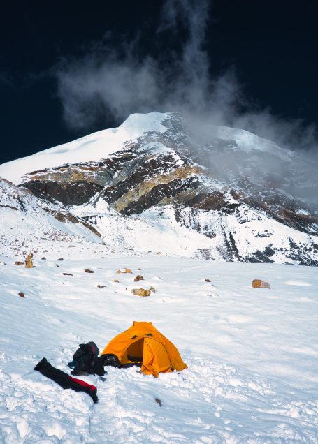 Zelt in schneebedecktem Gelände mit schneebedecktem Berg im Hintergrund.