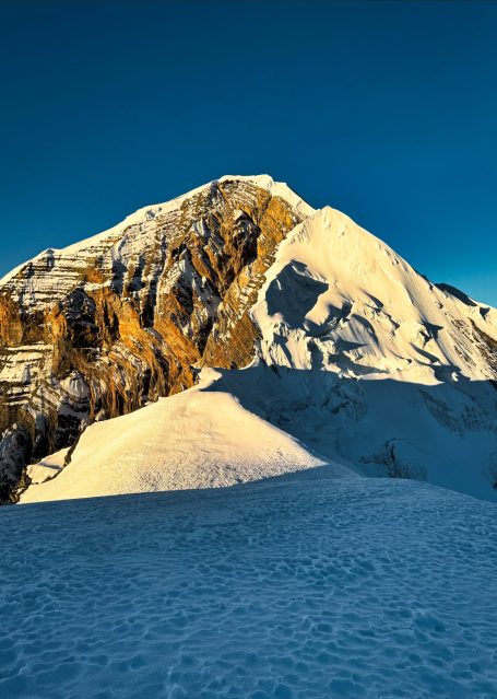 Schneebedeckter Berggipfel im Sonnenlicht mit klarem blauem Himmel.