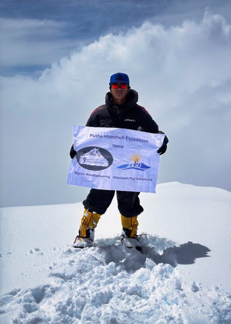 Person steht auf einem schneebedeckten Gipfel und hält ein Banner hoch.