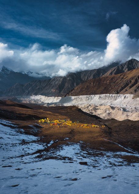 Berglandschaft mit Schnee, bunten Blumen und dramatischem Himmel.