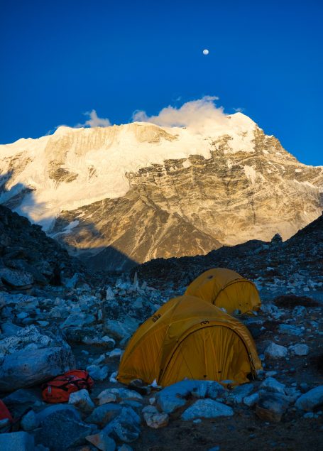 Zwei gelbe Zelte stehen vor einem schneebedeckten Berg unter einem klaren, blauen Himmel.