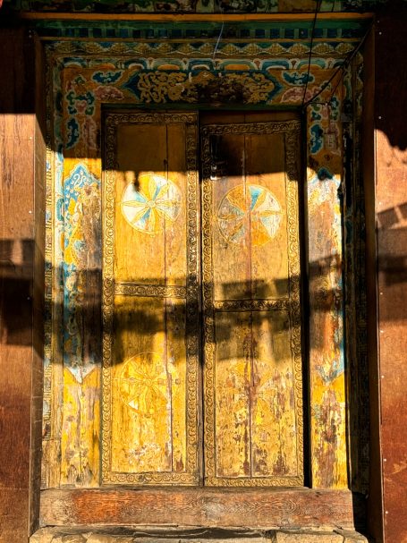 Detailreiche, kunstvoll verzierte Holztür mit bunten Mustern und Schattenwurf.