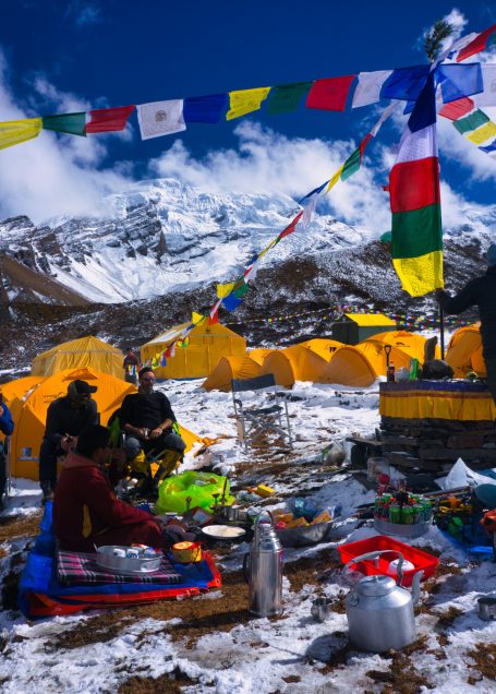 Bunte Gebetsfahnen und Zeltlager in schneebedeckter Berglandschaft.