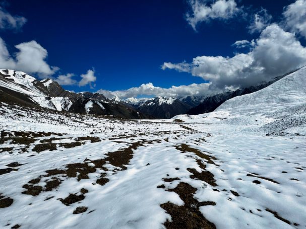 Weite, verschneite Landschaft mit Bergen und blauem Himmel, durchzogen von Wolken.