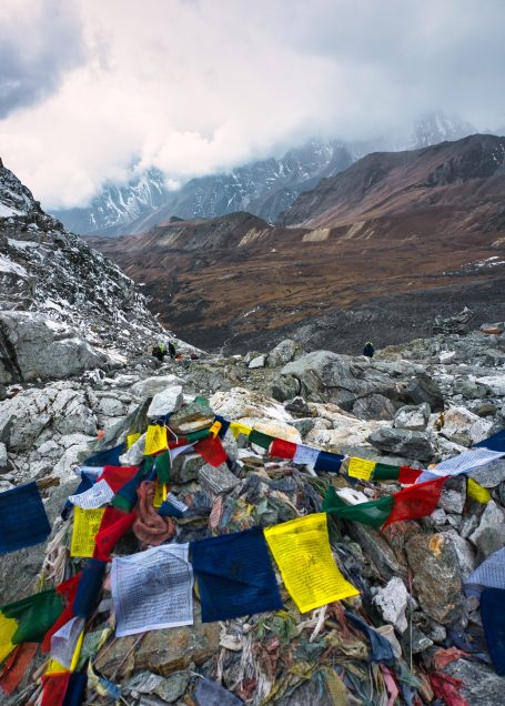 Bunten Gebetsfahnen liegen auf steiniger Fläche mit Bergen im Hintergrund.