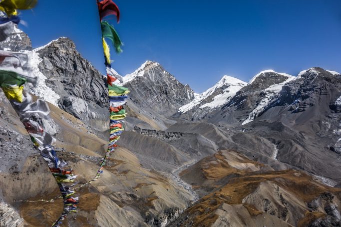 Berglandschaft mit schneebedeckten Gipfeln und bunten Gebetsfahnen im Vordergrund.