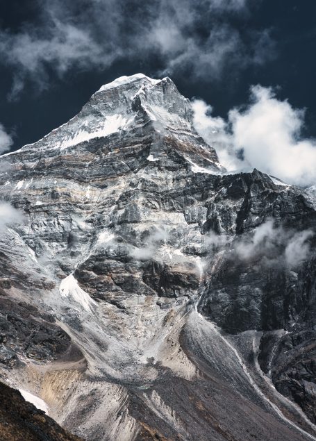 Hoher Berggipfel mit schneebedecktem Hang und dramatischer Wolkenbildung.
