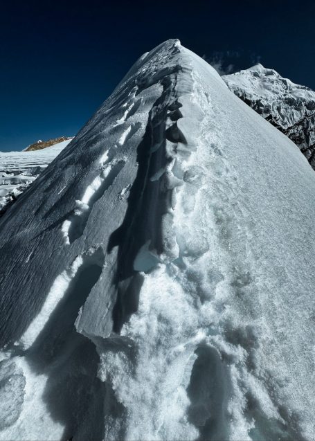 Schneebedeckte Bergspitze mit sichtbaren Fußspuren auf dem Weg nach oben.