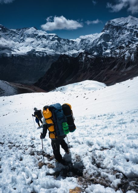 Bergsteiger mit Rucksack wandert durch schneebedeckte Landschaft mit Bergen im Hintergrund.