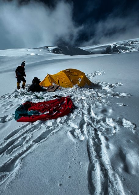 Zelt in verschneiter Landschaft, Fußspuren im Schnee, Person bereitet sich vor.