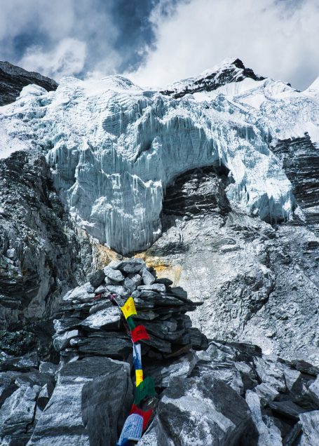 Schneebedeckte Berglandschaft mit bunten Gebetsfahnen und Gletscher im Hintergrund.