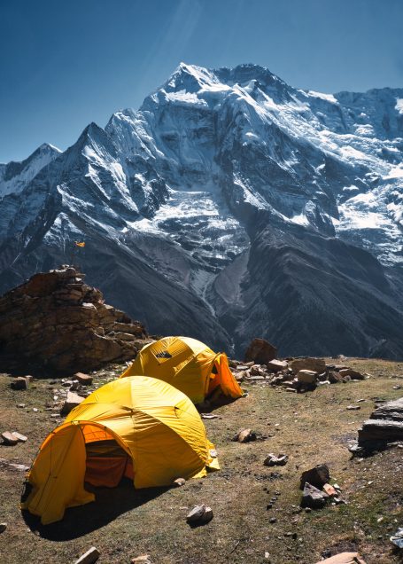 Zwei gelbe Zelte stehen in einer Berglandschaft mit schneebedeckten Bergen im Hintergrund.